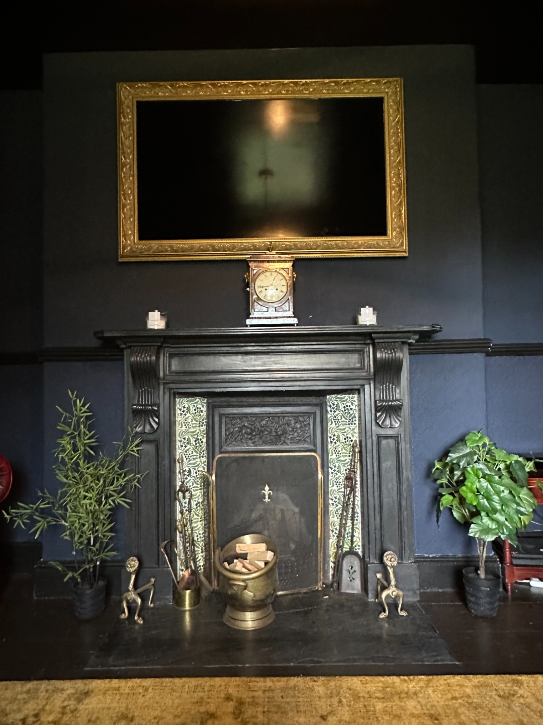 Ornate black fireplace, TV in gold frame, deep blue walls