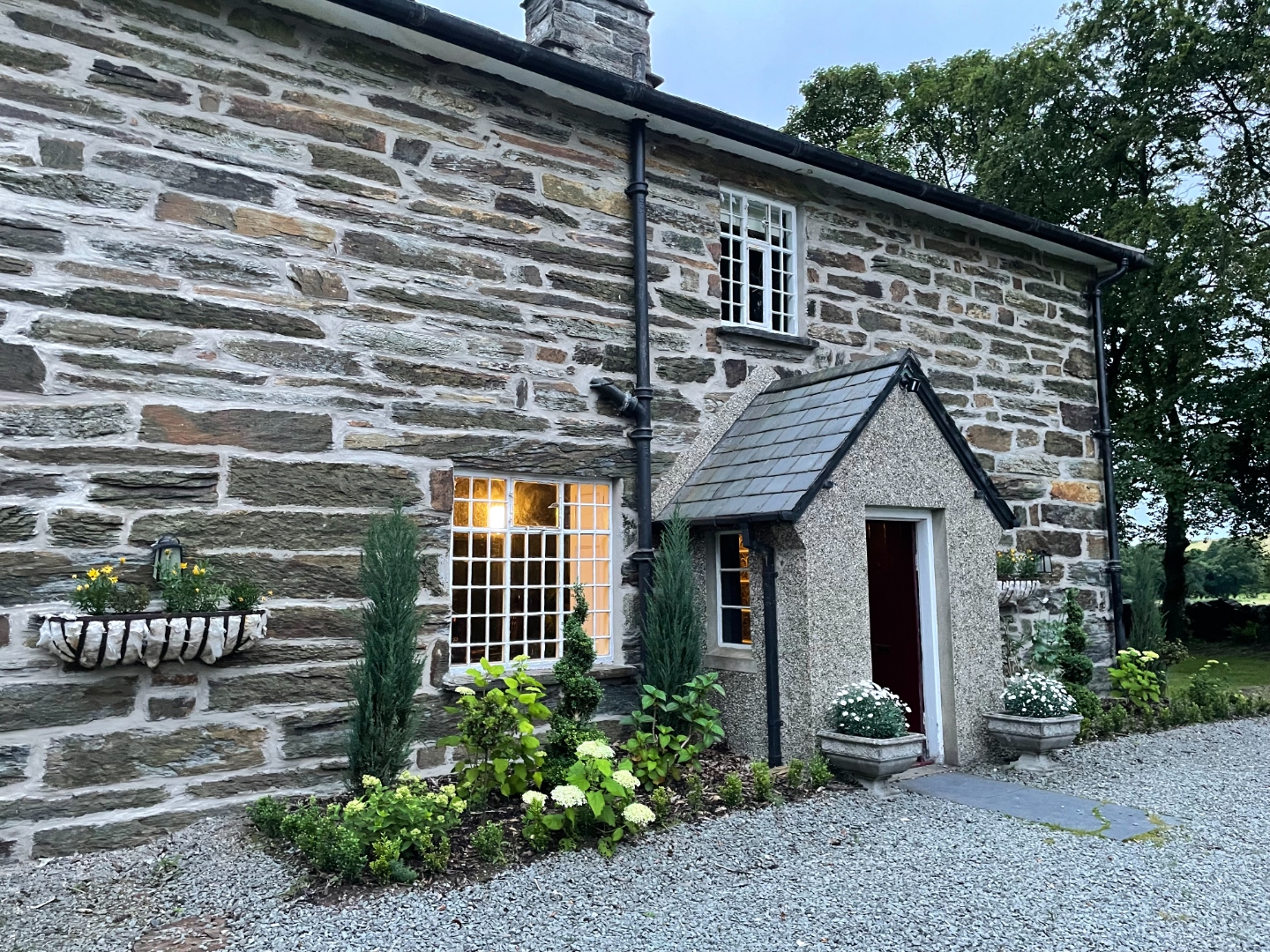 Front entrance of Tyddyn Eglwys showing the original Snowdonian stone walls, slate porch, and hydrangea plantings at dusk