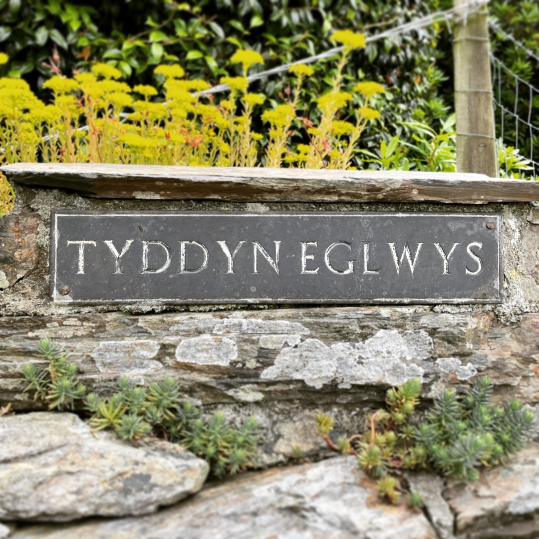 Slate name sign reading Tyddyn Eglwys on a stone wall
